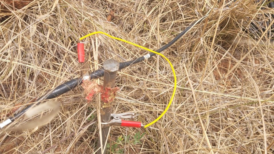 Eletrodo de aço cravado em capim seco com a garra vermelha e o fio amarelo ligados ao cabo da linha de Caminhamento Elétrico, em levantamento real da Aqua Liber