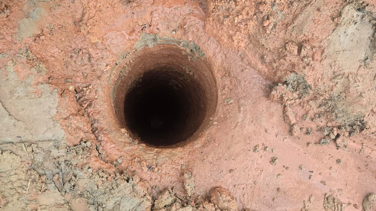 Boca de um poço tubular recém-perfurado em solo vermelho: um furo estreito, de poucas dezenas de centímetros, que desce dezenas de metros até o aquífero — bem diferente da boca larga de uma cacimba